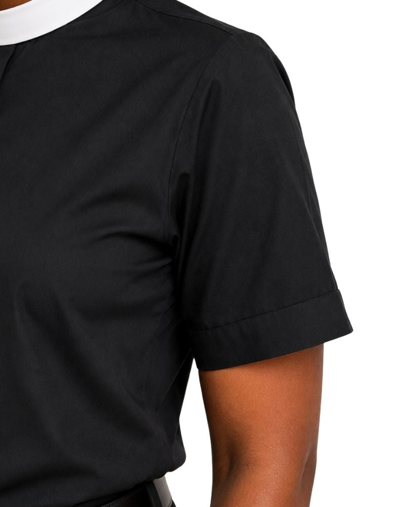 Close-up of a women wearing a black short-sleeve collared clerical shirt with a white collar trim, shown against a plain white background.