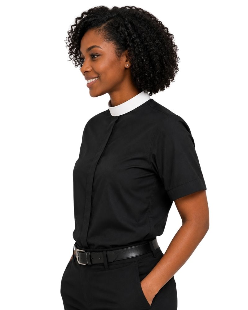 A woman with curly black hair is shown in profile wearing a black short-sleeve button-front clerical shirt with a contrasting white high collar, paired with black trousers and a black belt, against a plain white background.