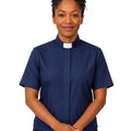 A woman wearing a navy blue short-sleeve clerical shirt with a white collar, standing against a plain white background.