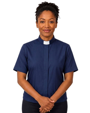 A woman wearing a navy blue short-sleeve clerical shirt with a white collar, standing against a plain white background.