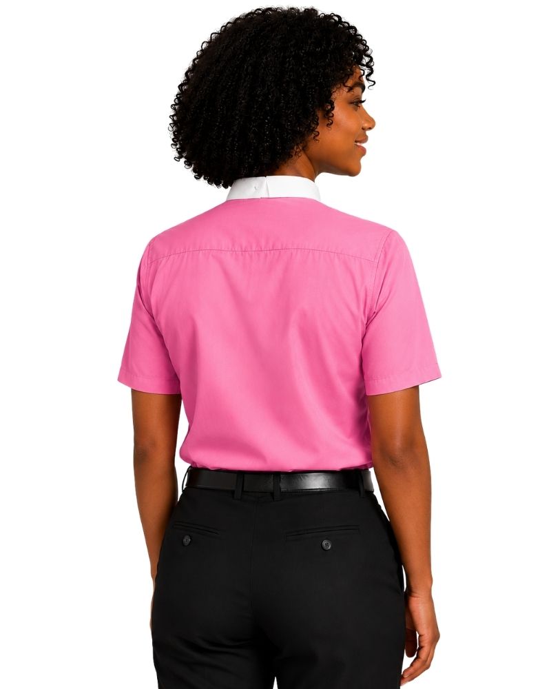 A woman shown from the back wearing a bright pink short-sleeve clerical shirt with a white collar, paired with black pants and a black belt, against a plain white background.