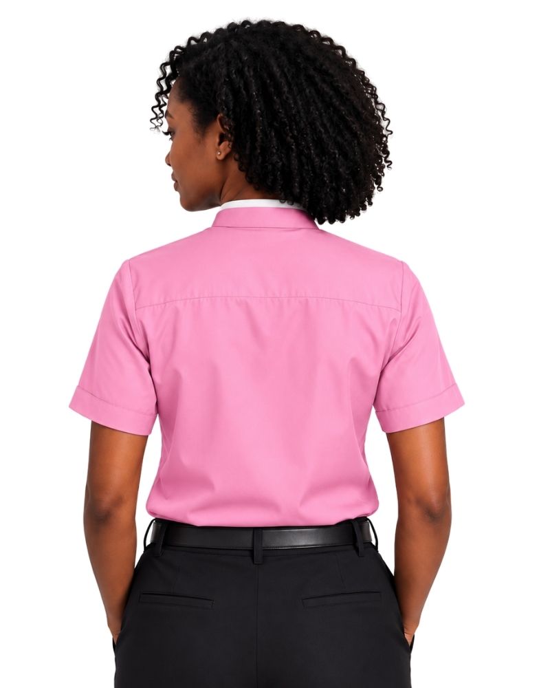 A woman shown from the back wearing a short-sleeve pink clerical shirt tucked into black trousers with a black belt, against a plain white background.