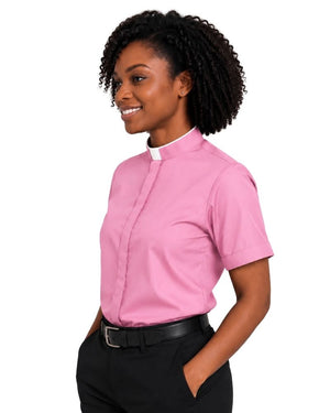 A woman wearing a pink short-sleeve clerical shirt with a white collar, paired with black trousers and a black belt, photographed against a solid white background.