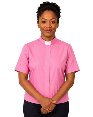A woman wearing a short-sleeve pink clerical shirt with a white collar, paired with black trousers, standing against a plain white background.