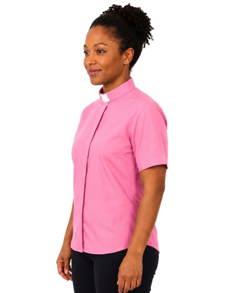 A woman wearing a short-sleeve pink clerical shirt with a white collar tab, shown in profile against a plain white background.
