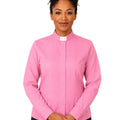 A woman wearing a pink long-sleeve clerical shirt with a white collar, standing against a plain white background.