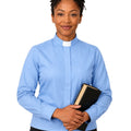 A woman modeling a light blue long-sleeve clerical shirt with a white collar, holding a black bibble against a plain white background.