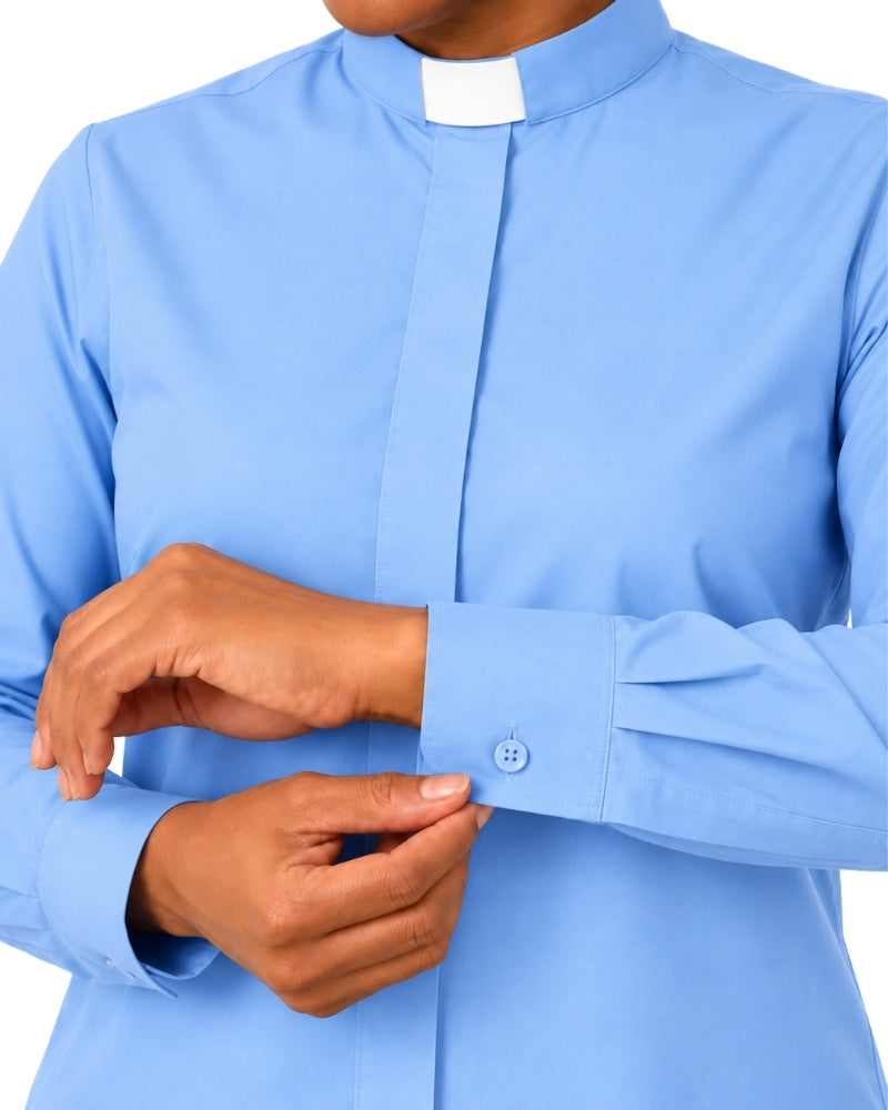 A close-up of a woman wearing a light blue long-sleeve clerical shirt with a white collar and adjusting the cuff.