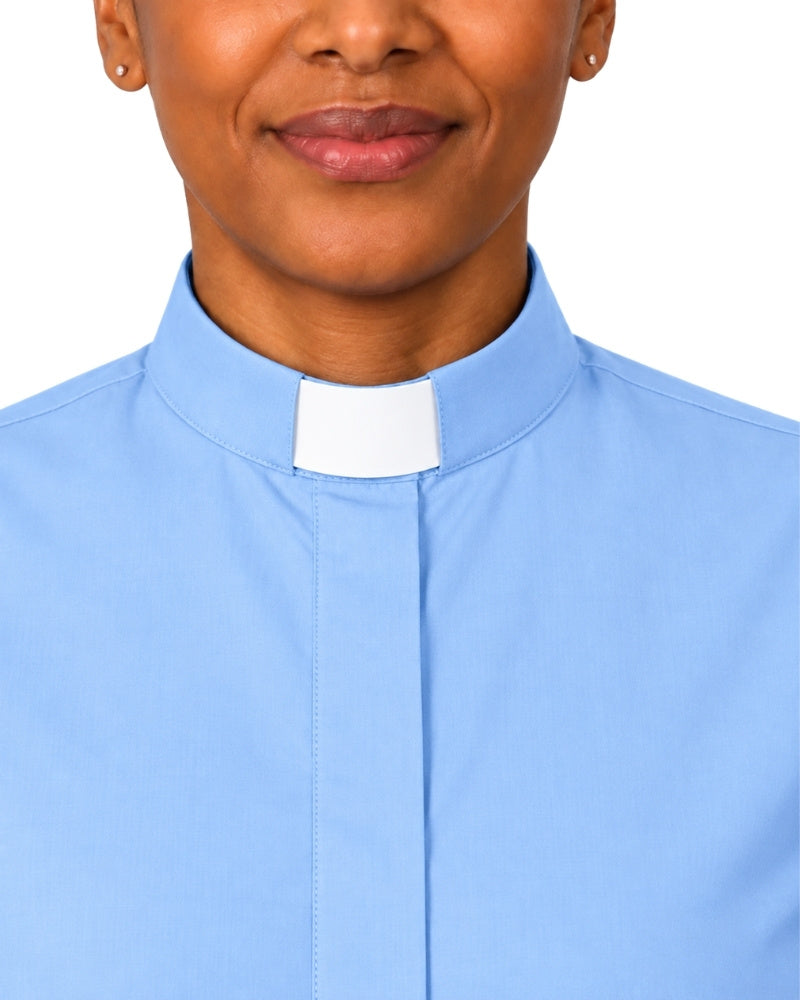 A close-up of a woman wearing a light blue clerical shirt with a white collar tab, shown against a plain white background.