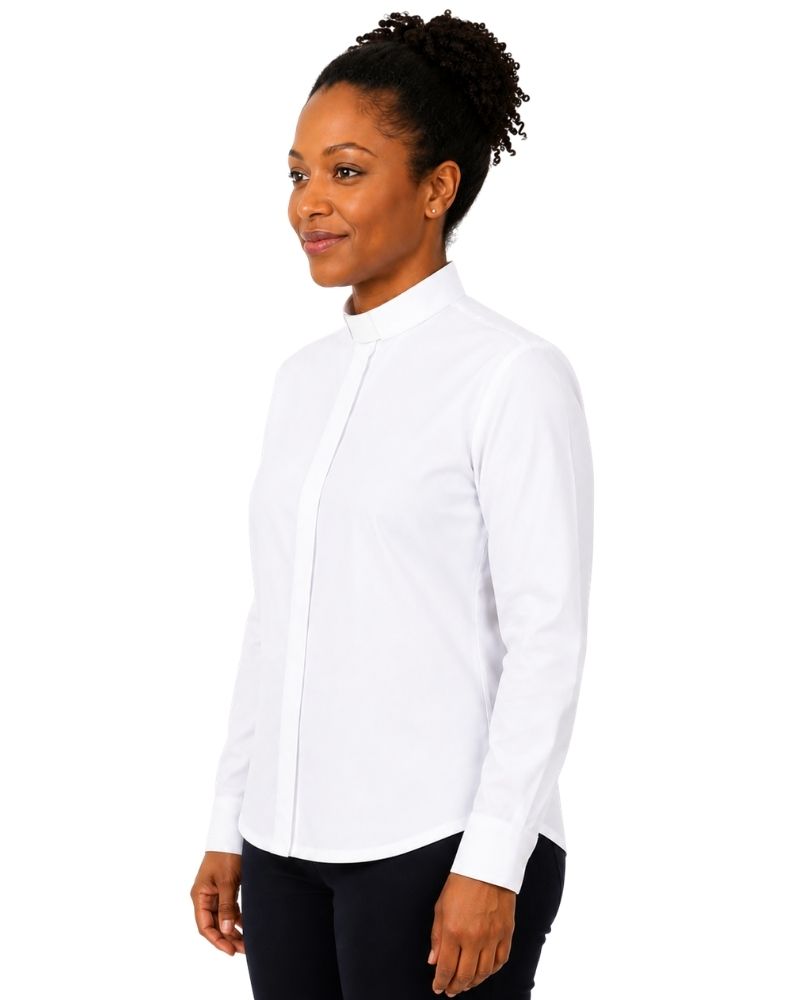 A woman wearing a white long-sleeve clerical shirt with a high mock neck, paired with black pants, photographed against a solid white background.