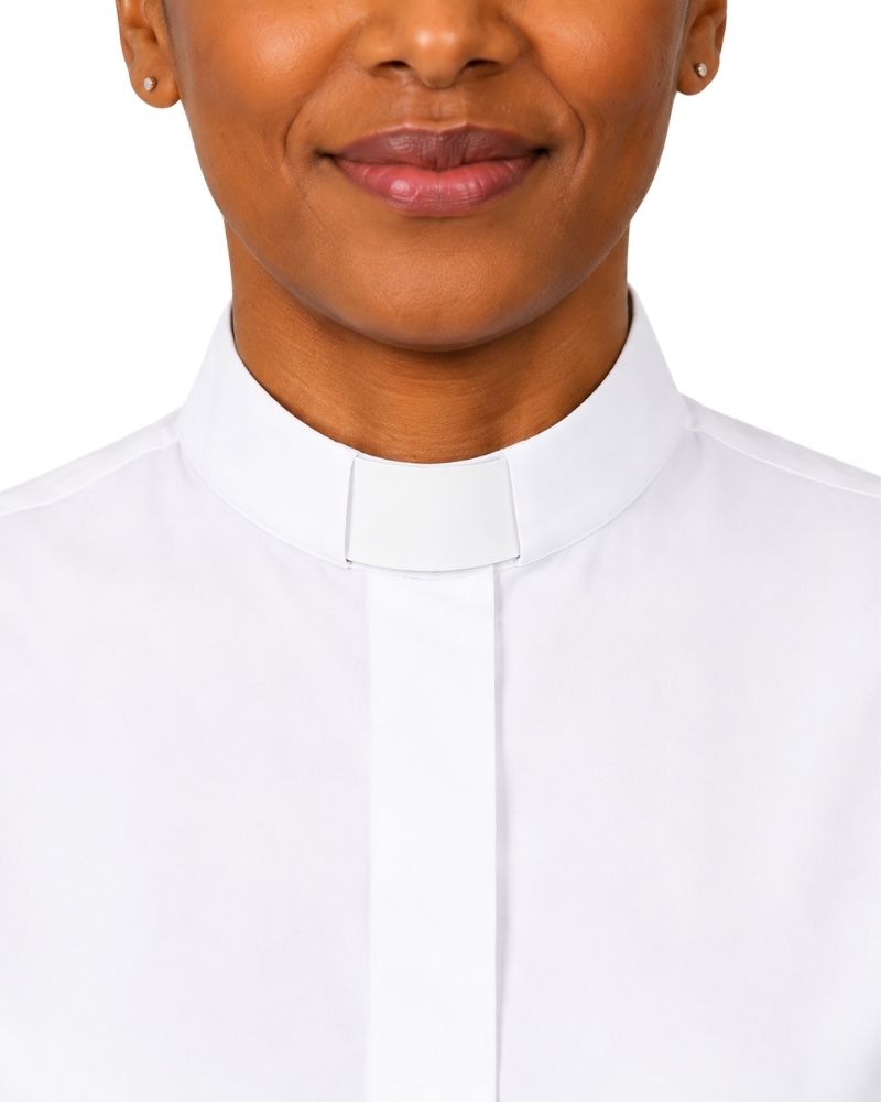 A close-up of a women wearing a white clerical collar shirt, showing the collar and upper chest against a plain white background.