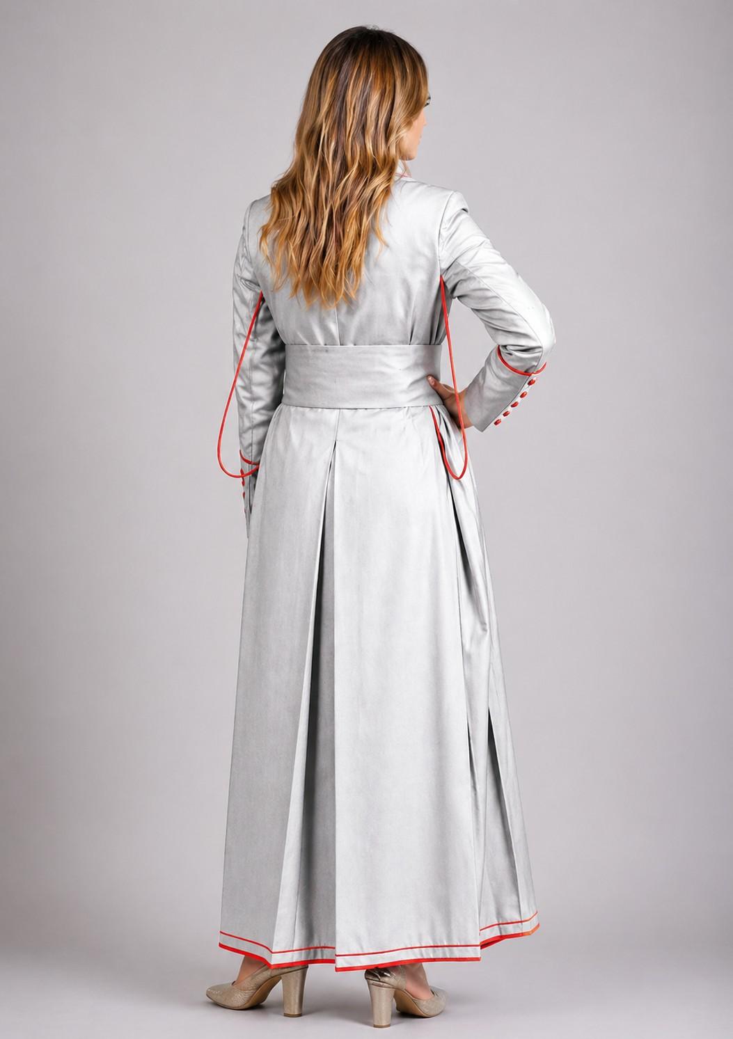 Woman wearing a long light gray dress with red trim on a plain background