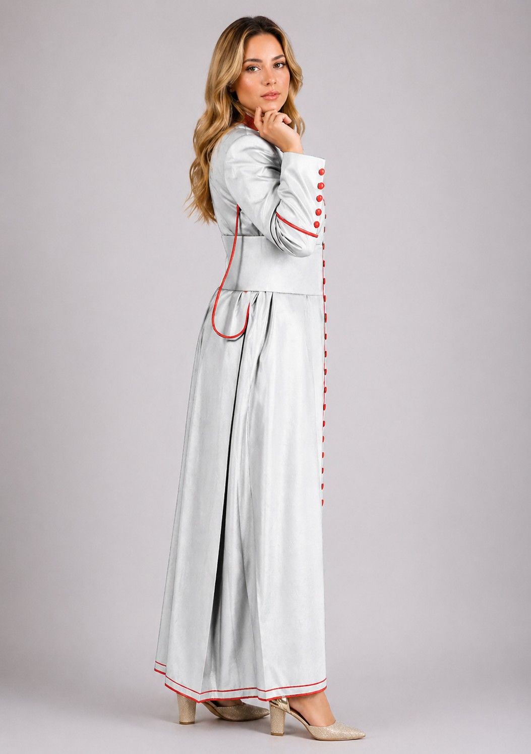 Woman wearing a long, light gray dress with red accents on a plain background