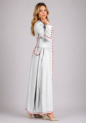 Woman wearing a long, light gray dress with red accents on a plain background