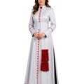 A woman modeling a long white cassock with red button details, red piping, and a red tassel accent, set against a plain white background.