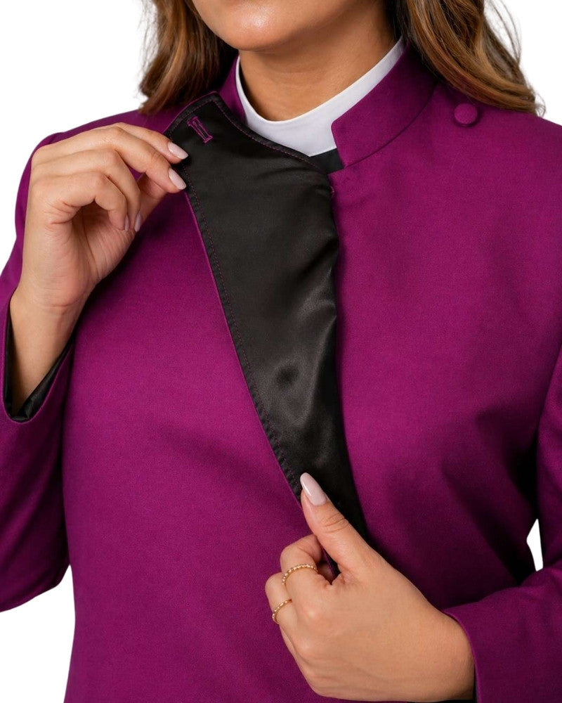 A close-up of a women wearing a magenta-purple cassock with a black satin lapel and a white collared shirt underneath, holding the lapel open.