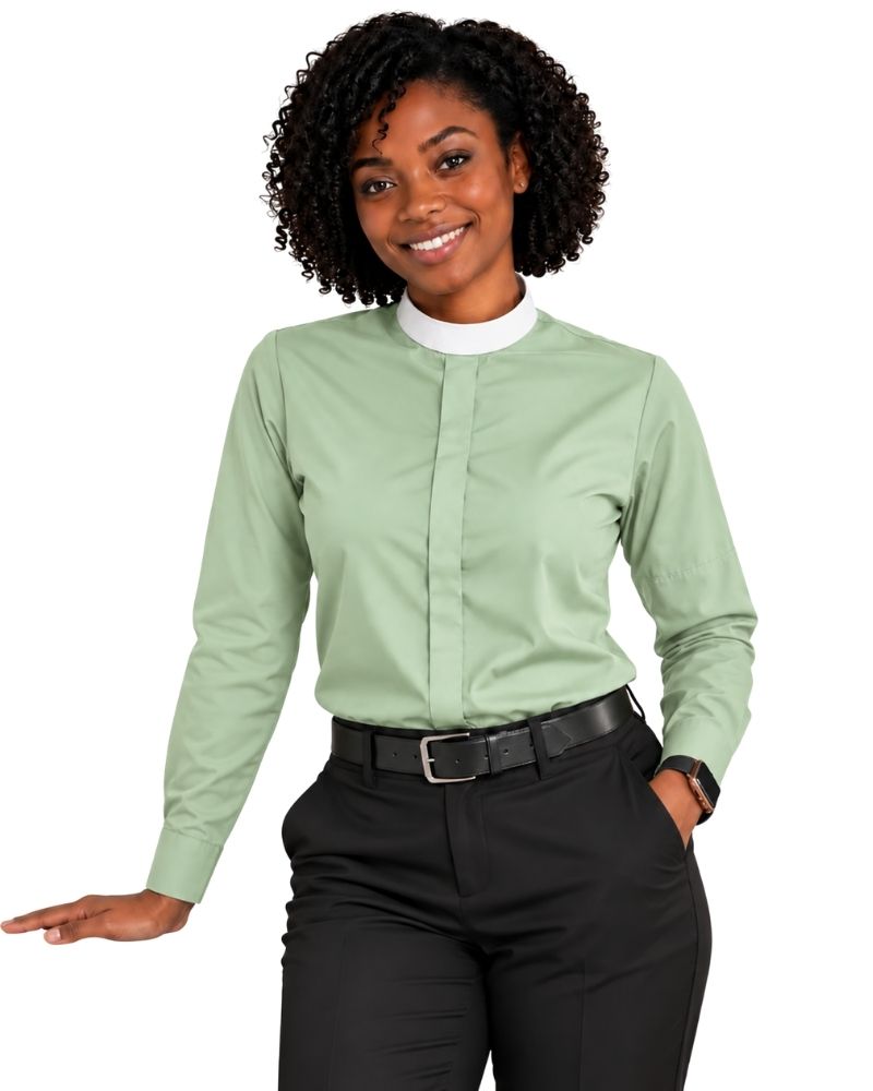 A woman modeling a sage green long-sleeve clerical shirt with a white mock neck collar, paired with black pants and a black belt, against a plain white background.