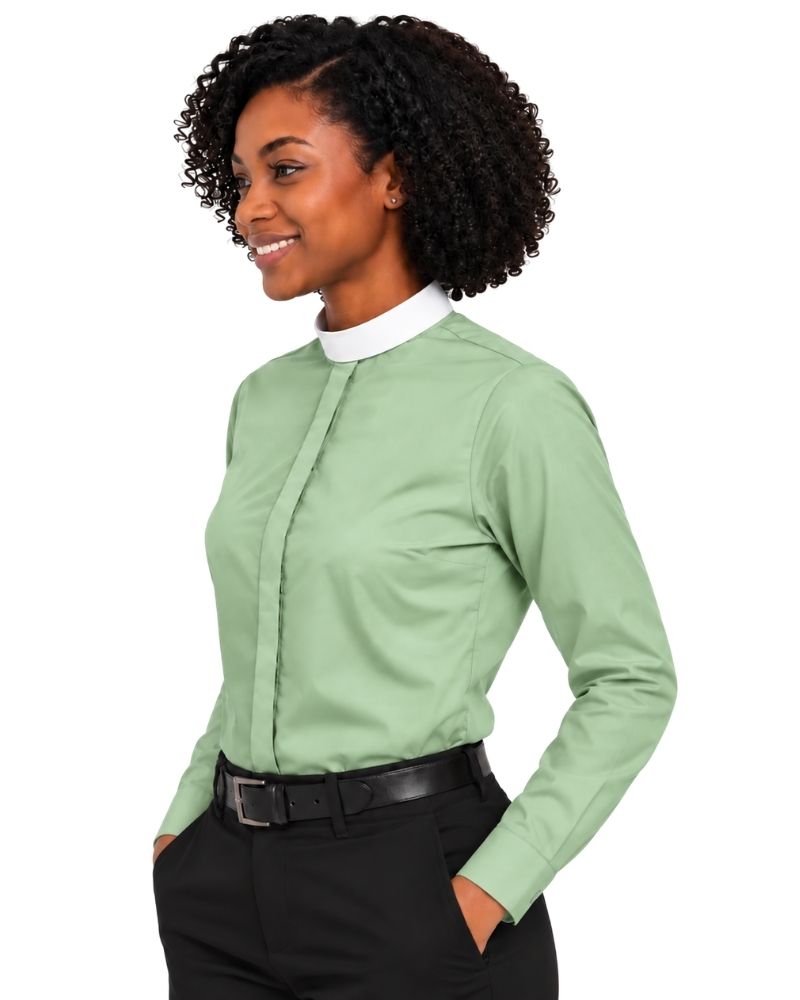 A woman modeling a sage green long-sleeve clerical shirt with a white mock neck collar, paired with black pants and a black belt, against a plain white background.