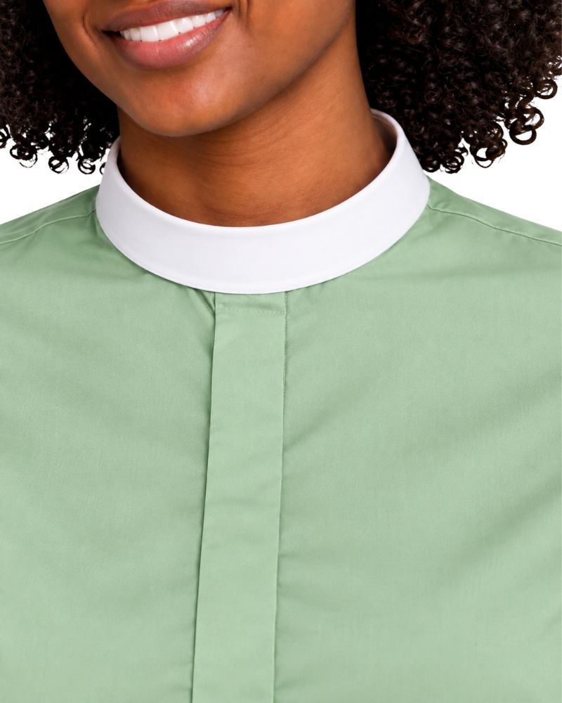 close up woman modeling a sage green short-sleeve clerical shirt with a white mock neck collar, against a plain white background.