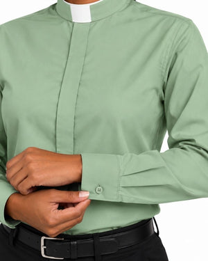 A close-up of a woman wearing a sage green long-sleeve clerical shirt with a white collar, adjusting the cuff with one hand and wearing a black belt with a silver buckle.