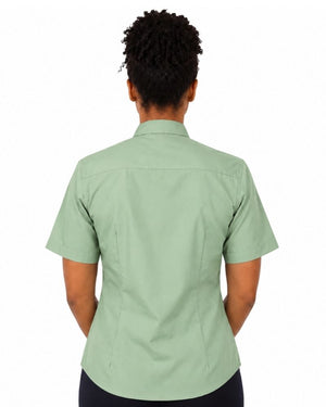 A woman viewed from the back wearing a light sage green short-sleeve clerical shirt, paired with black bottoms, against a plain white background.