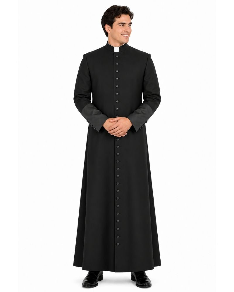 A man modeling a Black Roman Cassock with Satin Cuffs with a high stand collar, front button closure, and contrasting dark gray cuffs, shown against a plain white background.