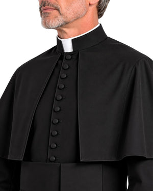 A close-up of a man wearing a black clerical cape with a high collar and a white clerical collar, set against a plain white background.
