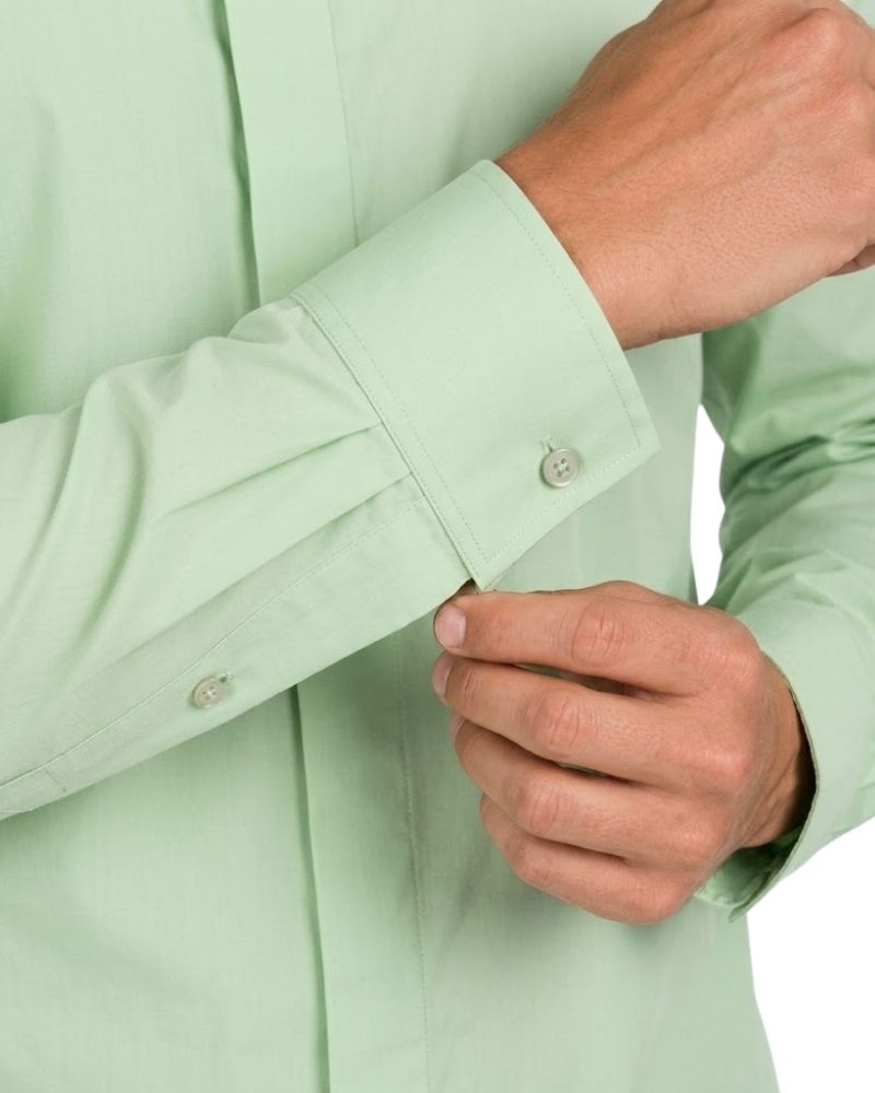 Close-up of a person wearing a light mint green clerical shirt, adjusting the cuff with one hand while the other hand is near the front button.