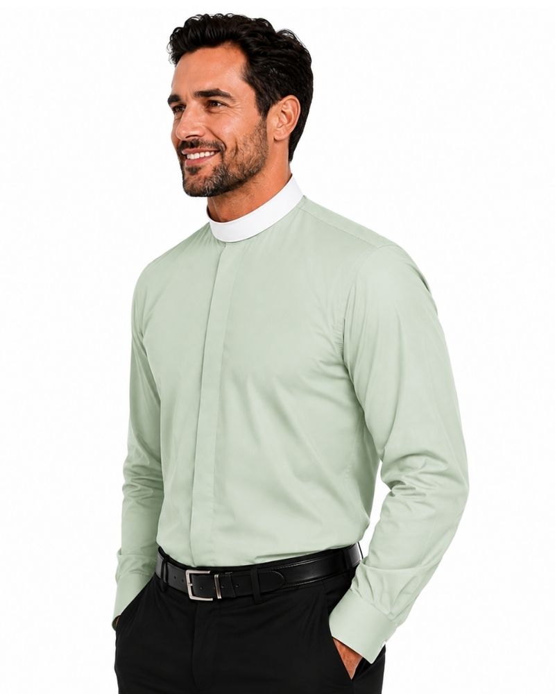 A man wearing a light sage green long-sleeve clerical shirt with a white mock neck collar, paired with black trousers and a black belt, against a plain white background.