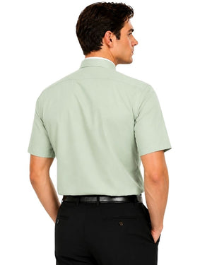 A man shown from the back wearing a light sage green short-sleeve clerical shirt with black trousers, photographed against a plain white background.