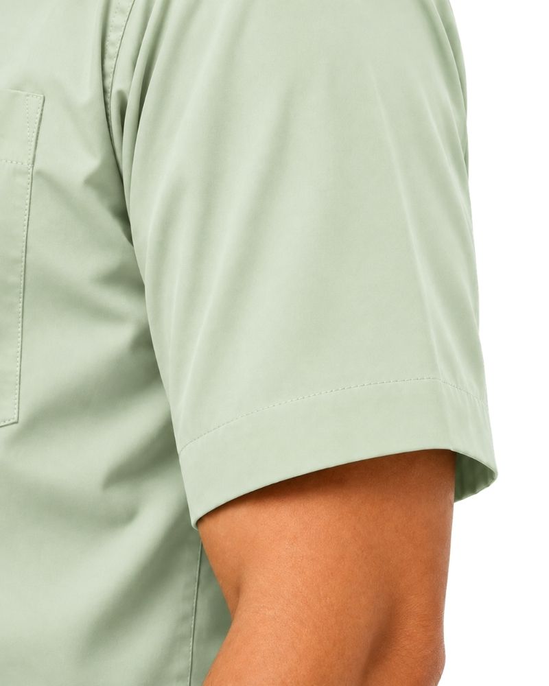 Close-up of a person wearing a light sage green short-sleeve clerical shirt, showing the sleeve cuff and part of the chest pocket against a white background.
