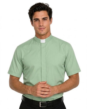 A man wearing a light sage green short-sleeve clerical shirt with a white collar tab, paired with black trousers and a black belt, against a plain white background.