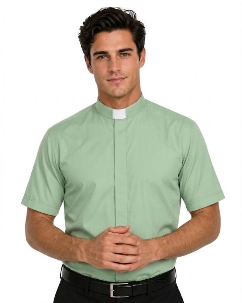 A man wearing a light sage green short-sleeve clerical shirt with a white collar tab, paired with black trousers and a black belt, against a plain white background.