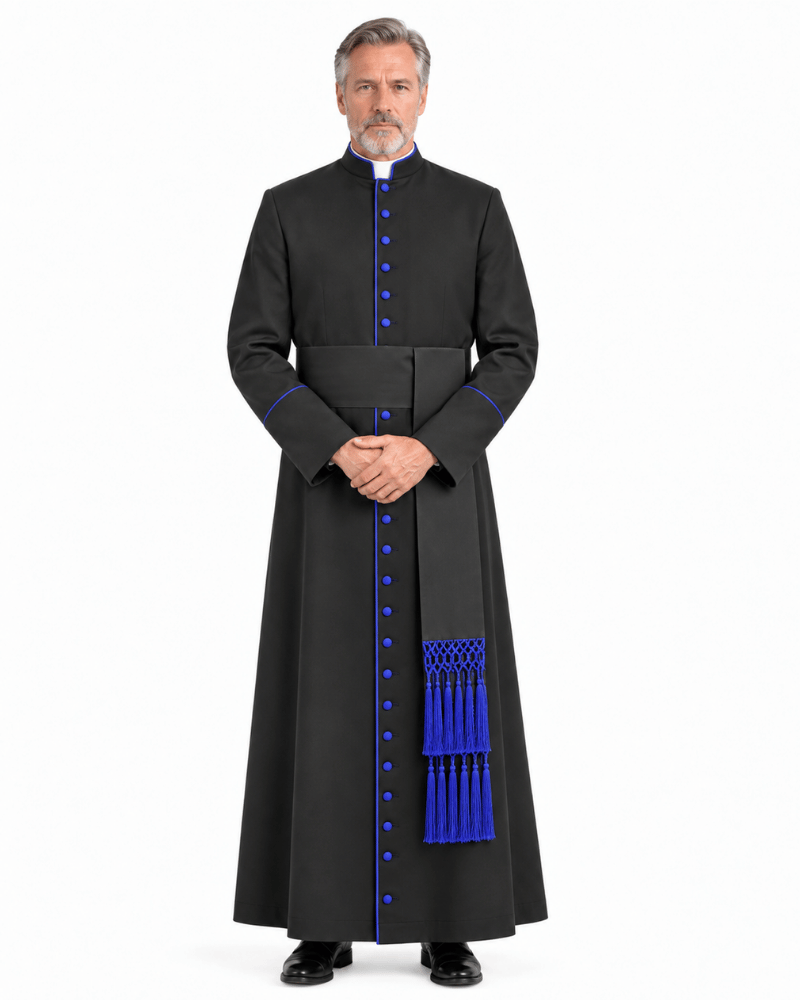 A man wearing a Obsidian Royal Blue Clerical Cassock with bright blue trim, blue buttons, and a matching blue sash with tassels, standing against a plain white studio background.