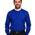 A smiling man wearing a royal blue long-sleeve clerical shirt with a white collar, paired with black trousers and a black belt, against a plain white background.