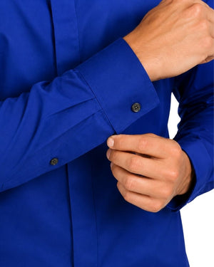 Close-up of a man wearing a bright royal blue clerical shirt and buttoning the cuff, with the hands and torso visible against a plain white background.