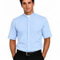 front side view of a man wearing a light blue short sleeve clergy shirt with a white tab collar, paired with black dress pants, shown on a professional studio white background.