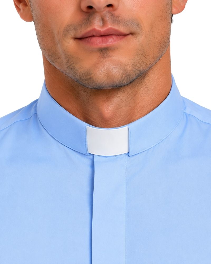 Closeup view of a man wearing a light blue short sleeve clergy shirt with a white tab collar, paired with black dress pants, shown on a professional studio white background.