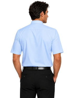 Back side view of a man wearing a light blue short sleeve clergy shirt with a white tab collar, paired with black dress pants, shown on a professional studio white background.