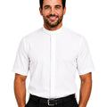 A man wearing a white short-sleeve clerical shirt with a high mock neck collar, paired with black trousers and a black belt, photographed against a solid white background.