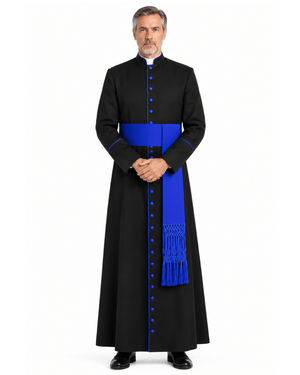 A man wearing a Black Clerical Cassock With Royal Blue Trim with a bright blue sash and matching blue buttons, standing against a plain white background.