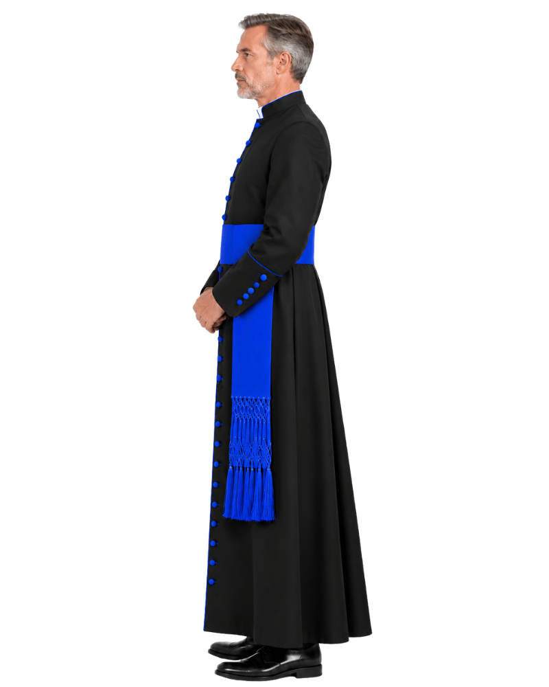 A man wearing a Black Clerical Cassock With Royal Blue Trim with vivid royal blue sash and matching blue decorative trim, photographed against a plain white studio background.