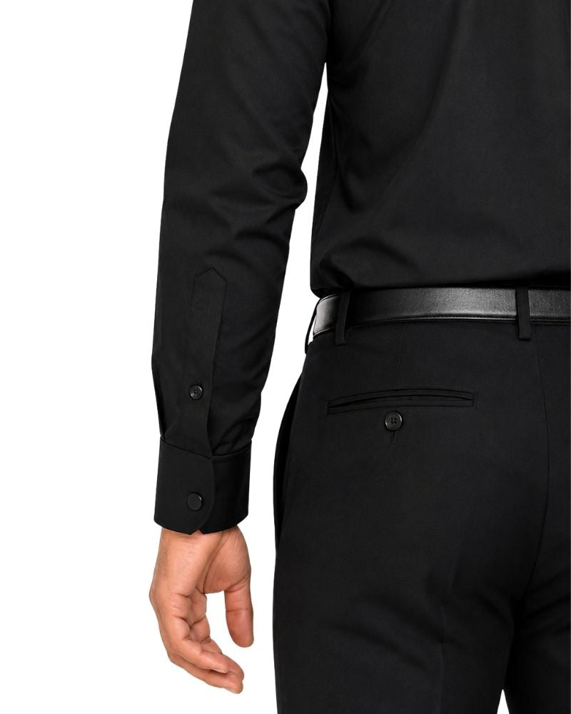 Close-up of a men wearing a black long-sleeve clerical shirt with buttoned cuffs, a black belt, and black trousers against a plain white background.