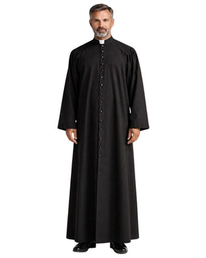 A man wearing a long black clerical robe with a high collar and a row of front buttons, standing against a plain white background.