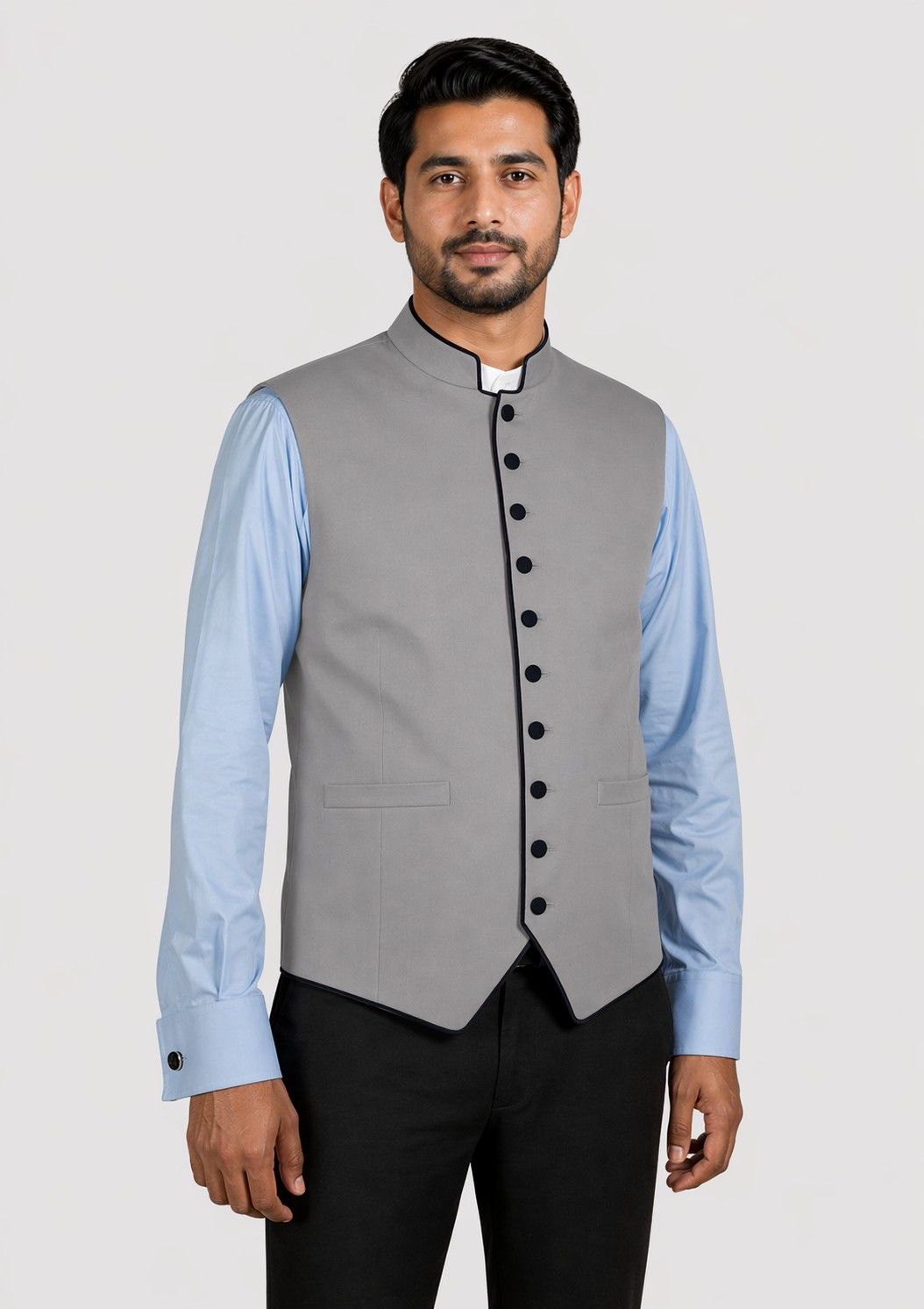 Man wearing a gray vest with black buttons over a light blue shirt with a white collar on a plain background