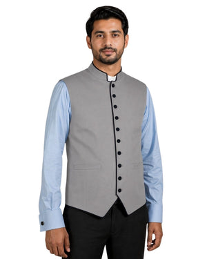 Man wearing a gray vest with black buttons over a light blue shirt on a white background.