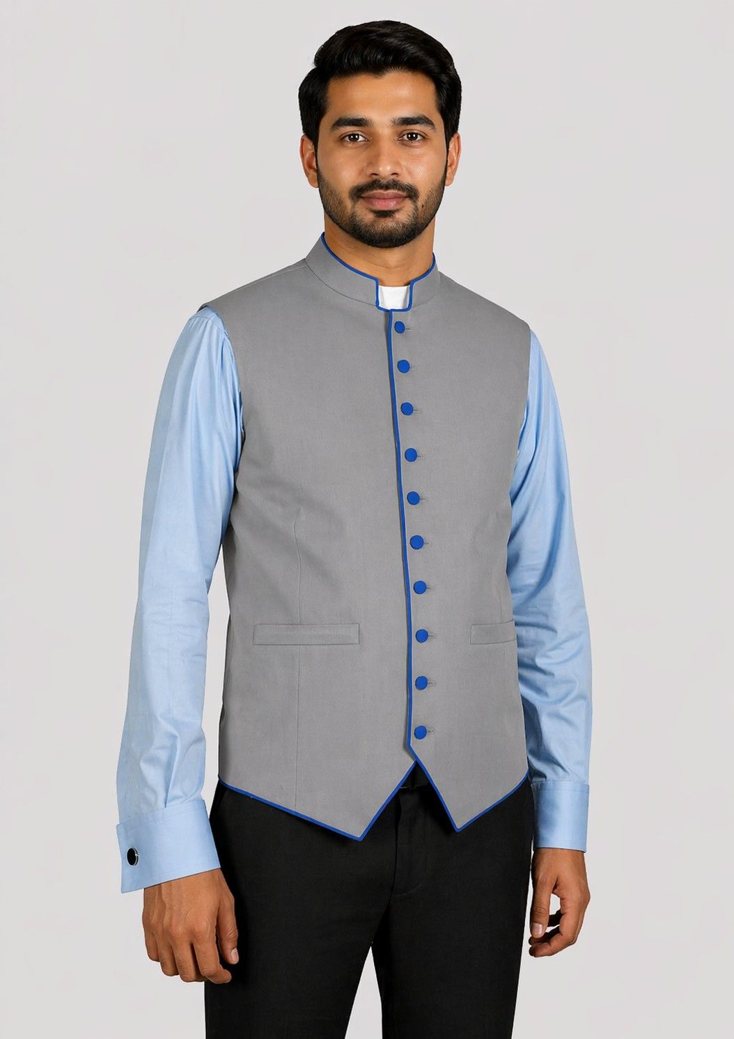 Man wearing a gray vest with blue buttons over a light blue shirt with a plain background