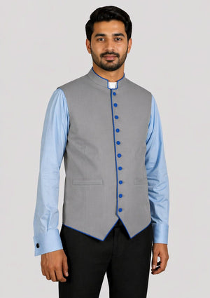 Man wearing a gray vest with blue buttons over a light blue shirt with a plain background