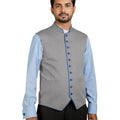 Man wearing a gray vest with blue buttons over a light blue shirt on a white background.