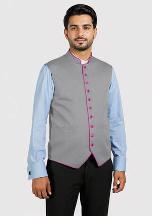 Man wearing a gray vest with pink buttons over a light blue shirt on a white background